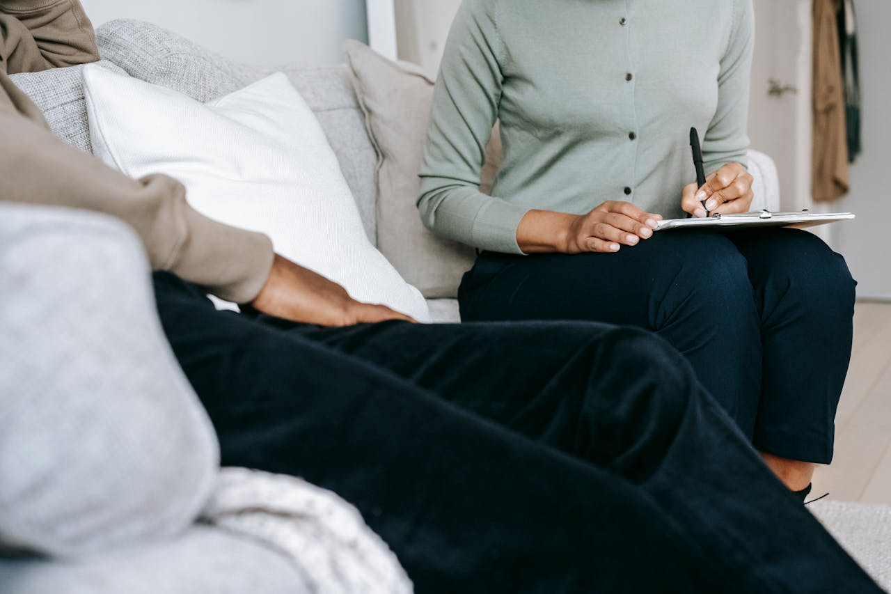 Crop anonymous female psychologist writing in clipboard and talking to black male client during psychotherapy appointment in light studio